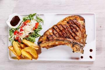 Bistecca di carne con cottura al sangue servita in una braceria con contorno di rucola, pomodori, salsa barbecue, formaggio a scaglie e patate al forno