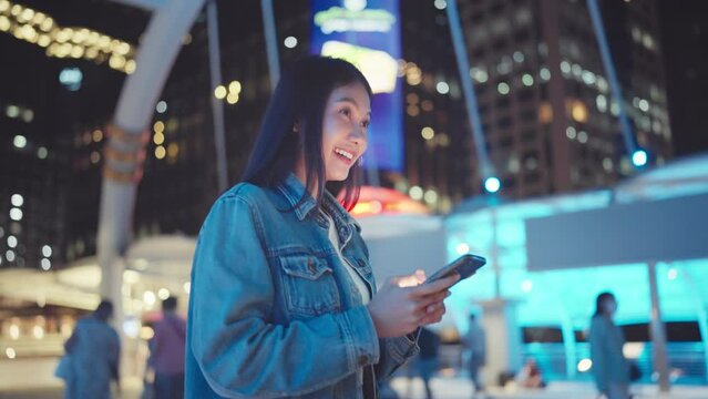 Happy asian woman with smile walking and using smartphone on the street in urban city, Smiling female checking message on mobile phone in town at night.