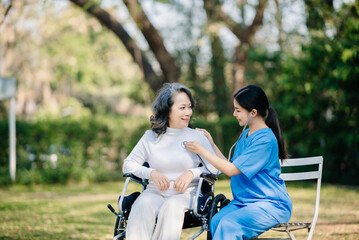Elderly asian senior woman on wheelchair with Asian careful caregiver. Nursing home hospital garden
