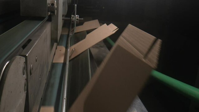 Automatic equipment folds carrying cardboard boxes in plant workshop closeup. Paperboard packaging production technology