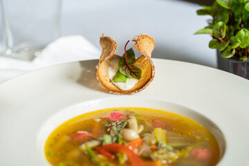 Selective focus of a special toasted bread variation with asparagus, baby swiss chard and white souce on the edge of plate. Vegetables soup in white plate.