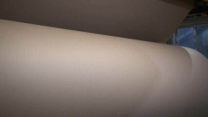 Unrolling huge roll with brown paper in manufacturing plant workshop closeup. Recycling papermaking factory technology at work