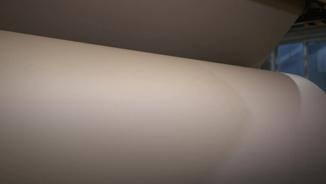 Unrolling huge roll with brown paper in manufacturing plant workshop closeup. Recycling papermaking factory technology at work