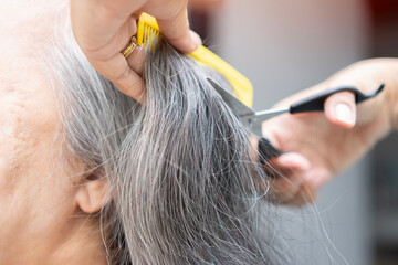 Closeup of hands of hairdresser on old woman with gray hairs.