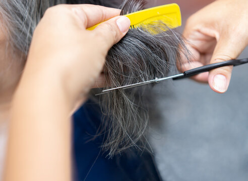 Cropped image of hands working with hair scissors. Professional hairstyler woman cutting hair of mature woman.