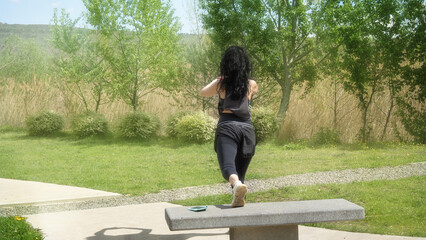 Young slim woman doing exercises in the park with a bench.