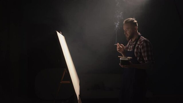Male artist creating a masterpiece of painting working in a dark creative studio looking for an idea. Concept of creativity and leisure