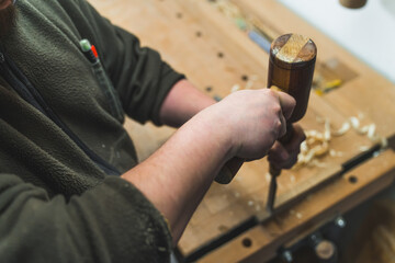 Carpenter using a chisel and a hammer to carve wood on a carpentry workbench. High quality photo