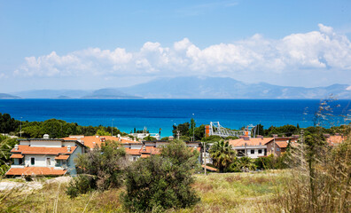 Fototapeta na wymiar View of the Aegean town in Turkey, blue sea, white clouds on the sky, grass and houses 