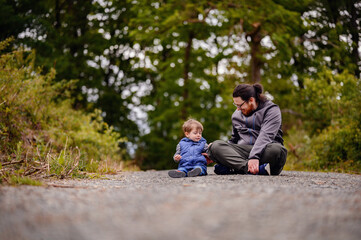 Young long hair bearded man in glasses sitting with little toddler boy on road playing with stones