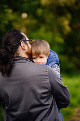 Fototapeta premium Young long hair bearded man in glasses holding little toddler boy on arms in green parks