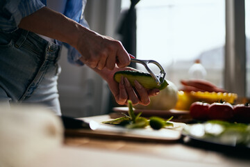 Female person peeling off a cucumber with a peeler tool in a home kitchen in the morning. Woman preparing fresh green salad for lunch