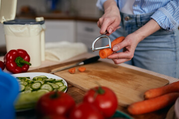 Woman preparing vegetarian salad at home. Female person peeling off a carrot with a peeler tool and recycling leftovers in a compost bin. Sustainable and healthy lifestyle concept