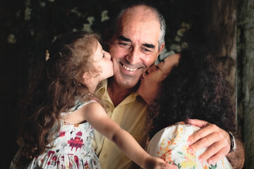 3 generations lifestyle portrait shot - a woman and her daughter kissing the father / grandfather - white Caucasian family celebrating a happy moment of affection
