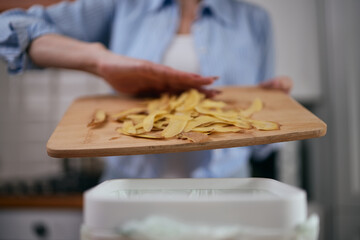 Woman throwing food scraps in a compost bin in close up. Responsible female person recycling...
