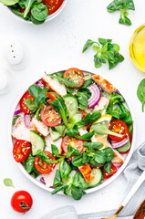 Healthy fresh salad with grilled chicken slice with cherry tomatoes, cucumber, red onion, lamb lettuce and sesame seeds on white table background, top view