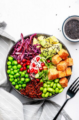 Healthy vegan food. Buddha bowl with quinoa, fried tofu, avocado, edamame, green peas, radish, cabbage and sesame seeds. White kitchen table background, top view