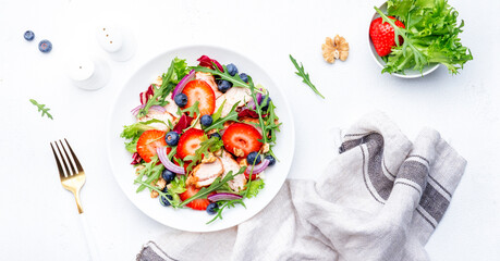 Summer strawberry and grilled chicken healthy salad with arugula, blueberries, red onion and walnuts, white table. Fresh useful dish for healthy eating