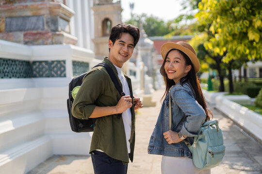 Portrait Of Asian Man And Woman Travel Couple Backpackers In Relationship Inside Of Buddhist Temple On The Street In Bangkok, Thailand, Southeast Asia - Carefree And Happy Traveling Concept