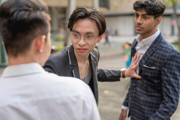 A young asian man gets in between 2 men fighting with each other and stops their quarrel. Trying to calm and reason with both people, and negotiating a truce.