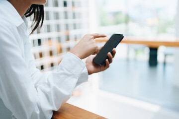 A young Asian self employed woman showing a smiling face and happiness while using smartphone mobile talking business and drinking coffee at a cafe shop. self-employed, freelance, relaxation.