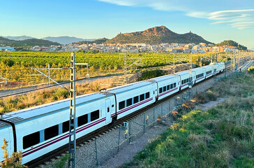 Train on railway on sunset in mountain. Speed train in motion on Valencia railroad. European passenger train on railway. High-speed train. Spanish National Rail Network.