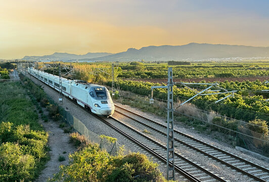 Train on railway on sunset in mountain. Speed train in motion on Valencia railroad. European passenger train on railway. High-speed train. Spanish National Rail Network.