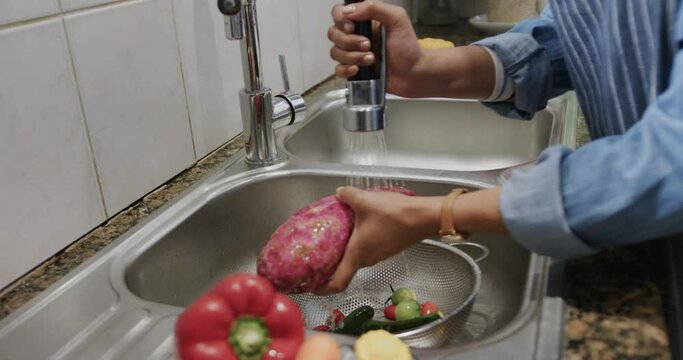 Hands of biracial woman washing vegetables in kitchen sink, slow motion