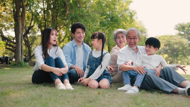 Asian family talking and sitting on grass in a park during summer morning, Relax time