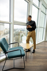 Obraz premium Dark-haired man with a phone in hands standing near the window