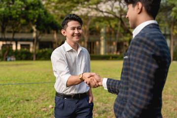 A young asian man shakes hands with an indian co-worker while outside the office.