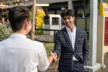 A young asian man shakes hands with an indian co-worker while outside the office.