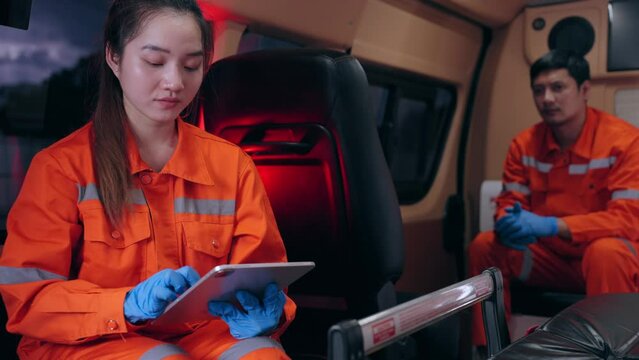 Emergency medical technician (EMT) Asian woman or paramedic using tablet and sitting in ambulance car while the car was going to the emergency location and turned on the siren light