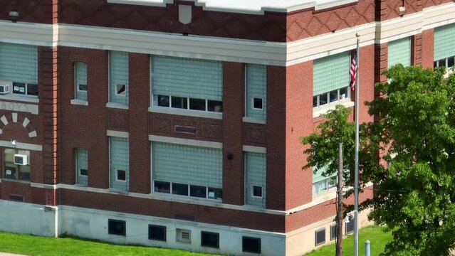 Aerial establishing shot of red brick school building in USA. American flag. Long zoom view on sunny day. Education in America theme.