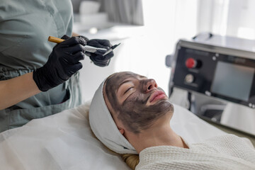 Dermatologist applies a green mask to the girl's face after cosmetic procedures, after carbon peeling. Mask rejuvenate the skin and stimulate the natural processes of cellular regeneration in clinic.