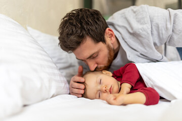 Fototapeta na wymiar Handsome brunette father kissing sleeping infant baby tenderly.