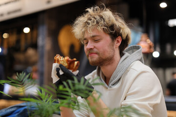 A bearded blond man rejoices at a burger in a restaurant.