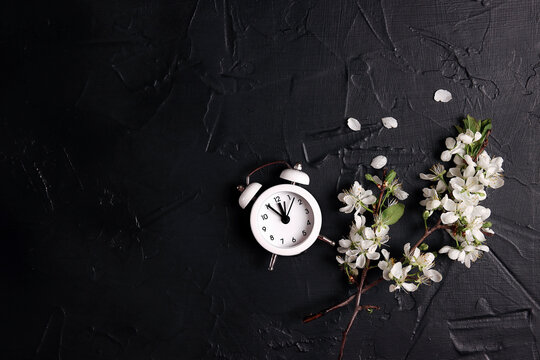 Small white alarm clock with apple blossom branches on a black background.