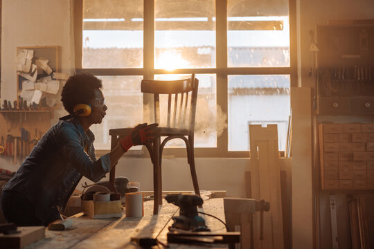 Woman carpenter sanding chair.