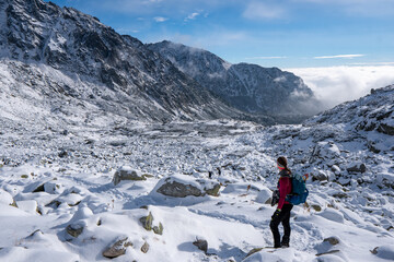 Hiker woman standing and looks around, admiring winter mountain landscape. Happy tourist woman in winter. High Tatras, 1987 meter above sea level. Slovakia - obrazy, fototapety, plakaty