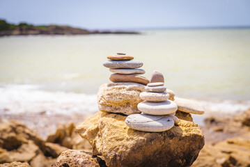 Balanced pebble pyramid on the beach on a sunny day. Abstract Sea bokeh on the background. Selective focus. Zen stones on the sea beach, meditation, spa, harmony, calmness, balance concept