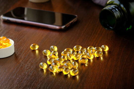Close-up of many omega-3 oil capsules on a dark brown table against the backdrop of a tablet container