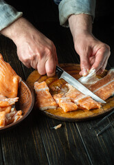 Cutting red fish on a kitchen cutting board before salting. Hands of a cook with a knife while cleaning a trout. The idea of a fish diet