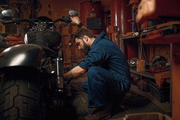 Fototapeta na wymiar Mechanic working with motorcycle engine in workshop while sitting nearby vehicle