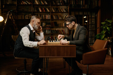 Side view on senior man and young guy chess player having friendly match at home