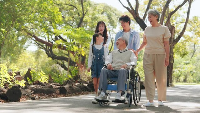 Happy Asian senior man sitting on wheelchair in the public park with big family on weekends holiday