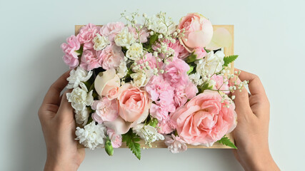 Hands holding wooden crate full of pastel colors flowers with pink rose and carnation on white background