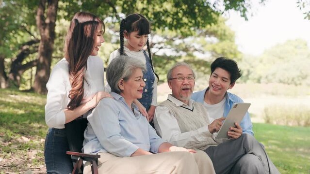Big Asian family  talking using tablet together and sitting under shade tree in the garden during autumn morning