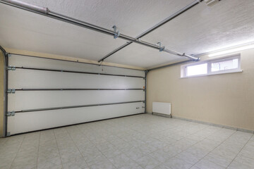 Modern garage with wide automatic gates. A clean room with light floor tiles and a window under the ceiling.