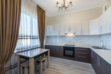 The interior of a modern kitchen. Dining table by the window with beautiful curtains. .Kitchen set in two contrasting colors.